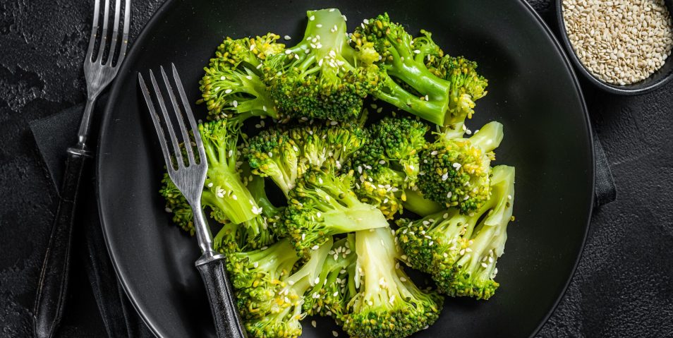 Boiled broccoli with spices in a plate. Black background. Top view Boiled broccoli with spices in a plate. Black background. Top view.